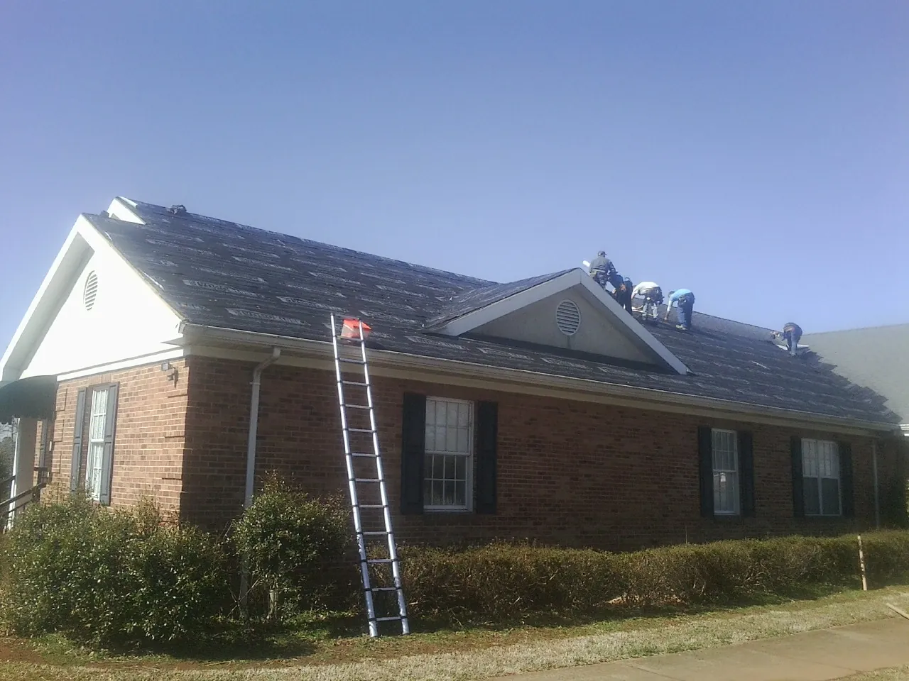 Crew tearing shingles off a brick ranch roof with a ladder set — Metal Roof Repair work by our crew in Stockholm