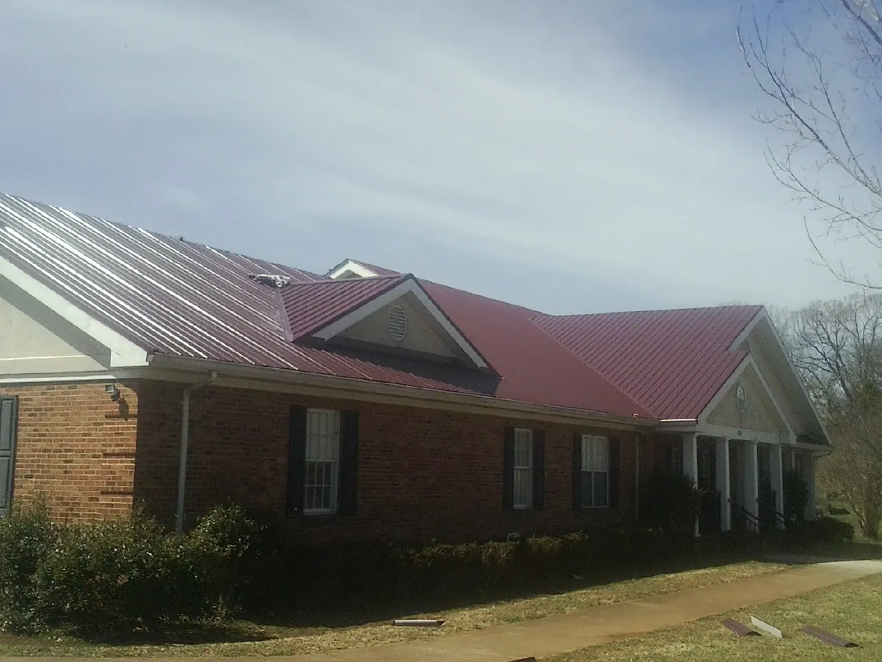 Red metal roof with gabled entries on a long brick building, from a Hail Damage Roof Repair job in Stockholm