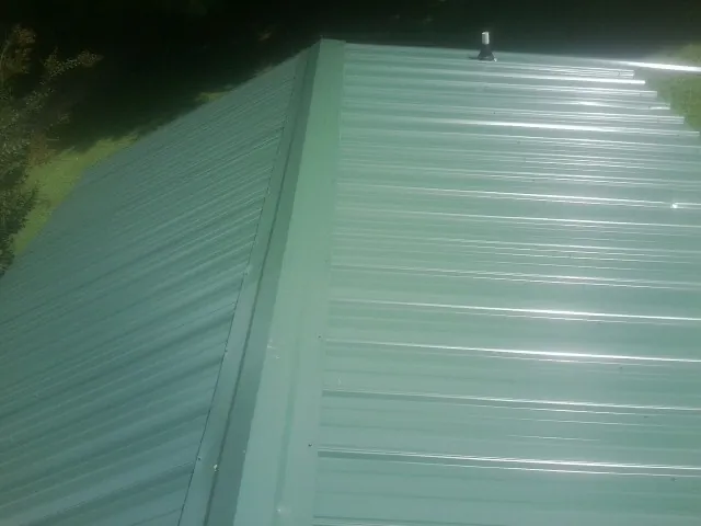New green metal panels meeting at the ridge of a roof — Flat Roof Repair work by our crew in Stockholm