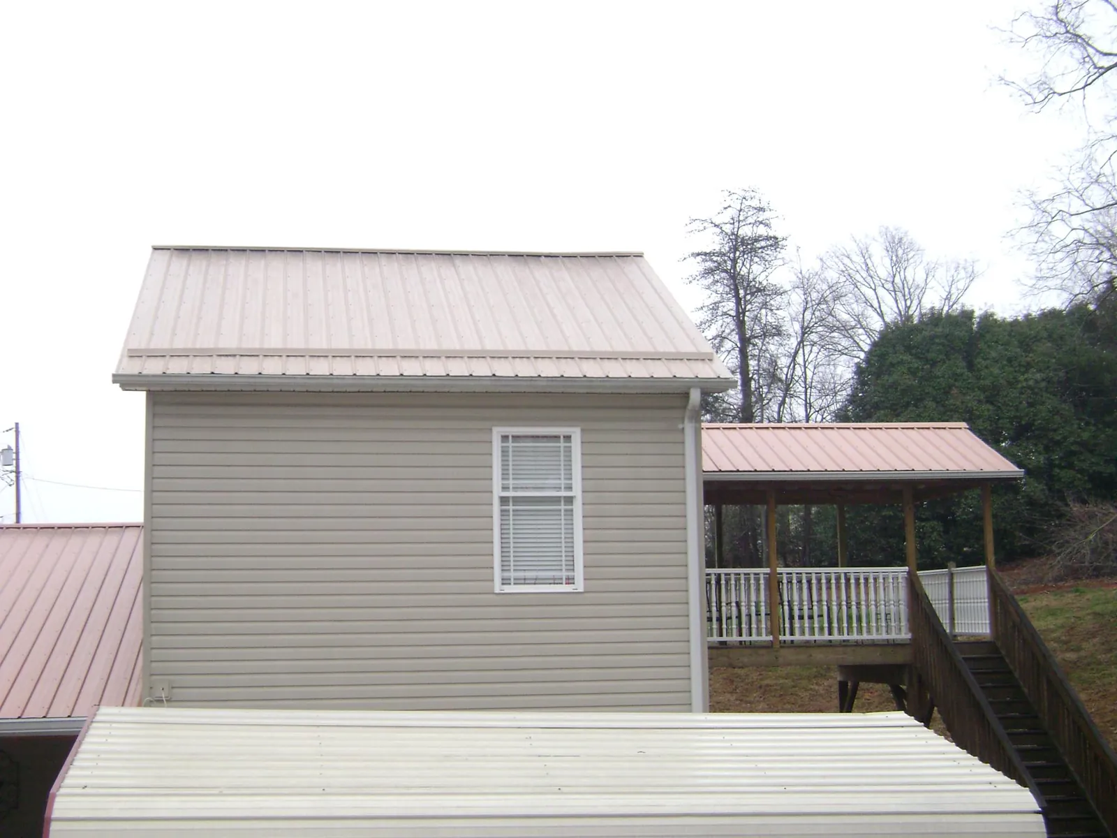 Tan metal roofs on a two story addition and attached porch, from a Roof Replacement job in Stockholm